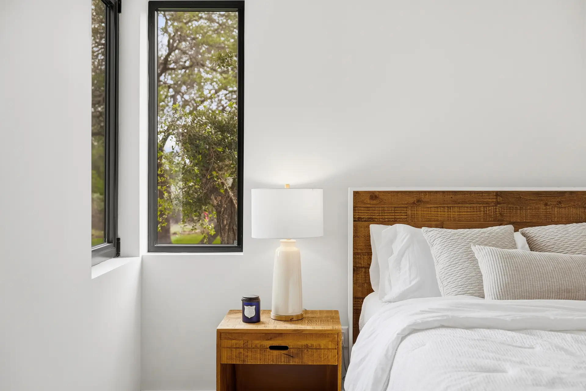 Bluewater Residence bedroom with reclaimed-wood headboard and tall window in Lago Vista, Texas